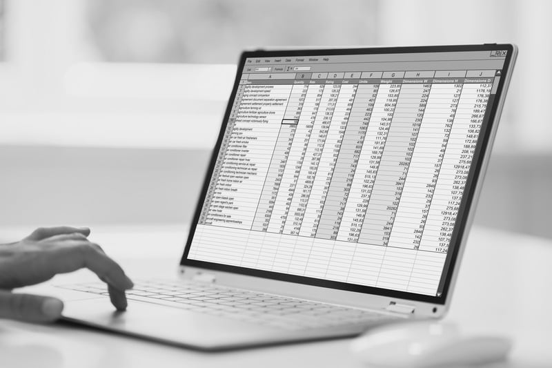 A hand using the trackpad of a laptop that is displaying a complex spreadsheet with multiple columns of data.