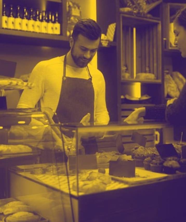 A smiling man wearing an apron serves a customer from behind a bakery counter
