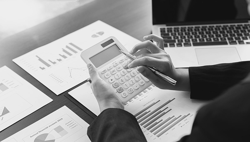 A person in a dark suit using a calculator with a pen in hand.