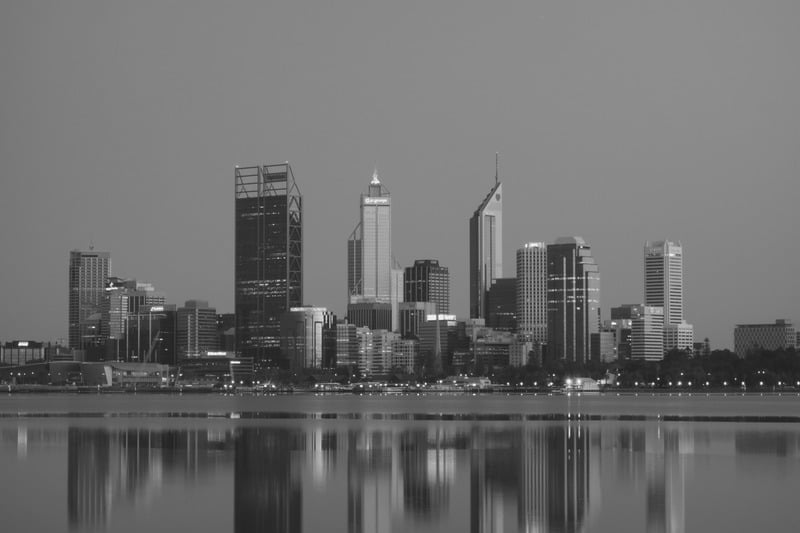 A city skyline reflected in the calm water of a foreground river at dusk.