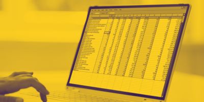 A person's hand typing on a laptop displaying a spreadsheet