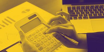 A person using a calculator and pen next to a laptop and financial charts.