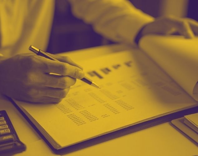 A close-up of a person's hands as they use a pen to point at data on a document