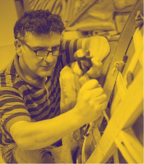 A man with glasses and a striped shirt using tools to work on a piece of furniture.