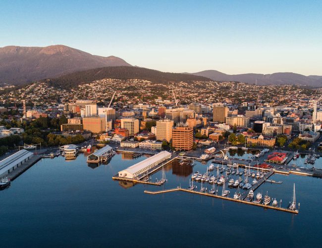 A coastal city harbor at dusk, featuring rows of sailboats in a marina